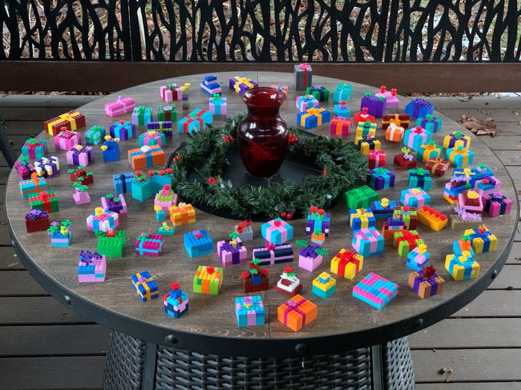 Over 100 colourful LEGO-built gifts on a round table with a green wreath  and red vase in the centre.