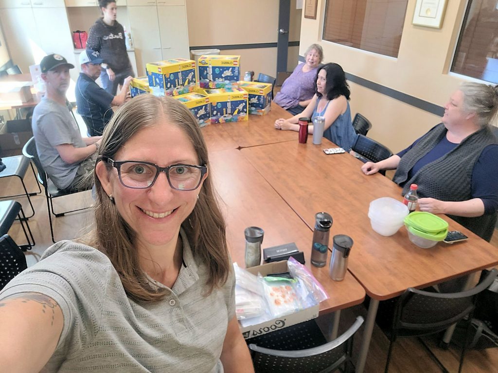 MILUG members sitting around a table with 8 boxes of the LEGO Classic Space sets stacked in the middle